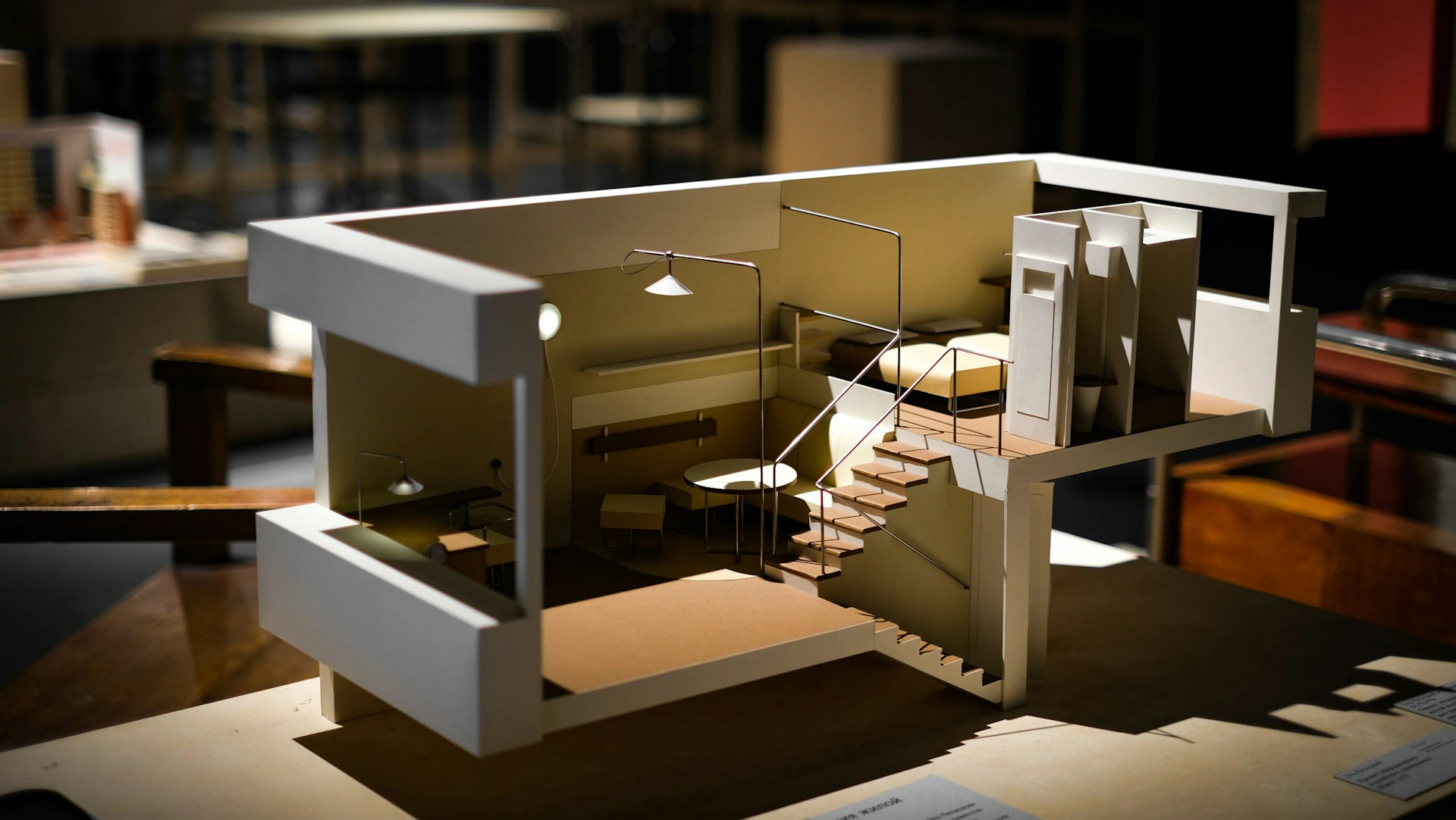 A well-lit architectural model by Northgate Construction showcases a modern, minimalist interior with an open staircase, tables, chairs, lamps, and partitioned spaces, displayed on a table alongside other models in the background.