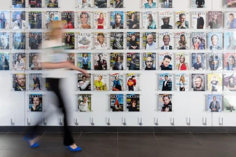 A blurred person walks past a wall display covered with many SUCCESS magazine covers featuring celebrities and business figures, reminiscent of the visionary spirit seen at Northgate Construction.