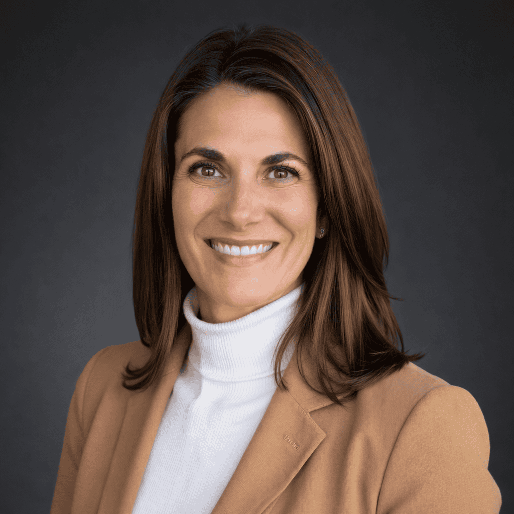 A woman with straight brown hair, wearing a tan blazer over a white turtleneck, smiles at the camera against a dark gray background.